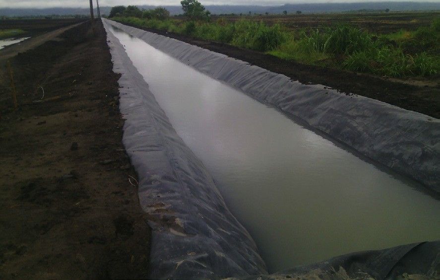 A long straight irrigation canal lined with black geomembrane and filled with water, between cultivated fields