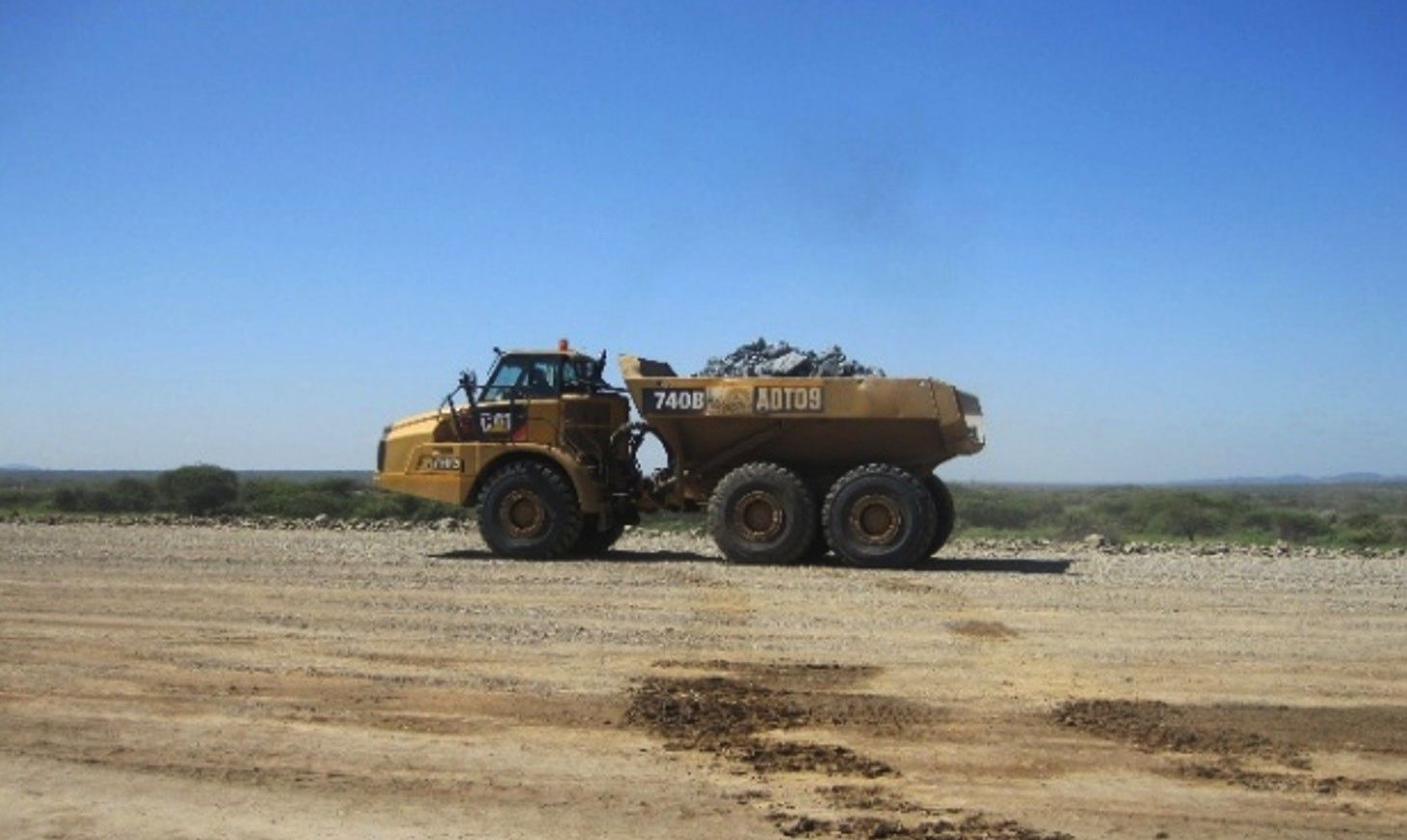 An articulated dump truck carrying rock across a flat earth platform under a clear blue sky