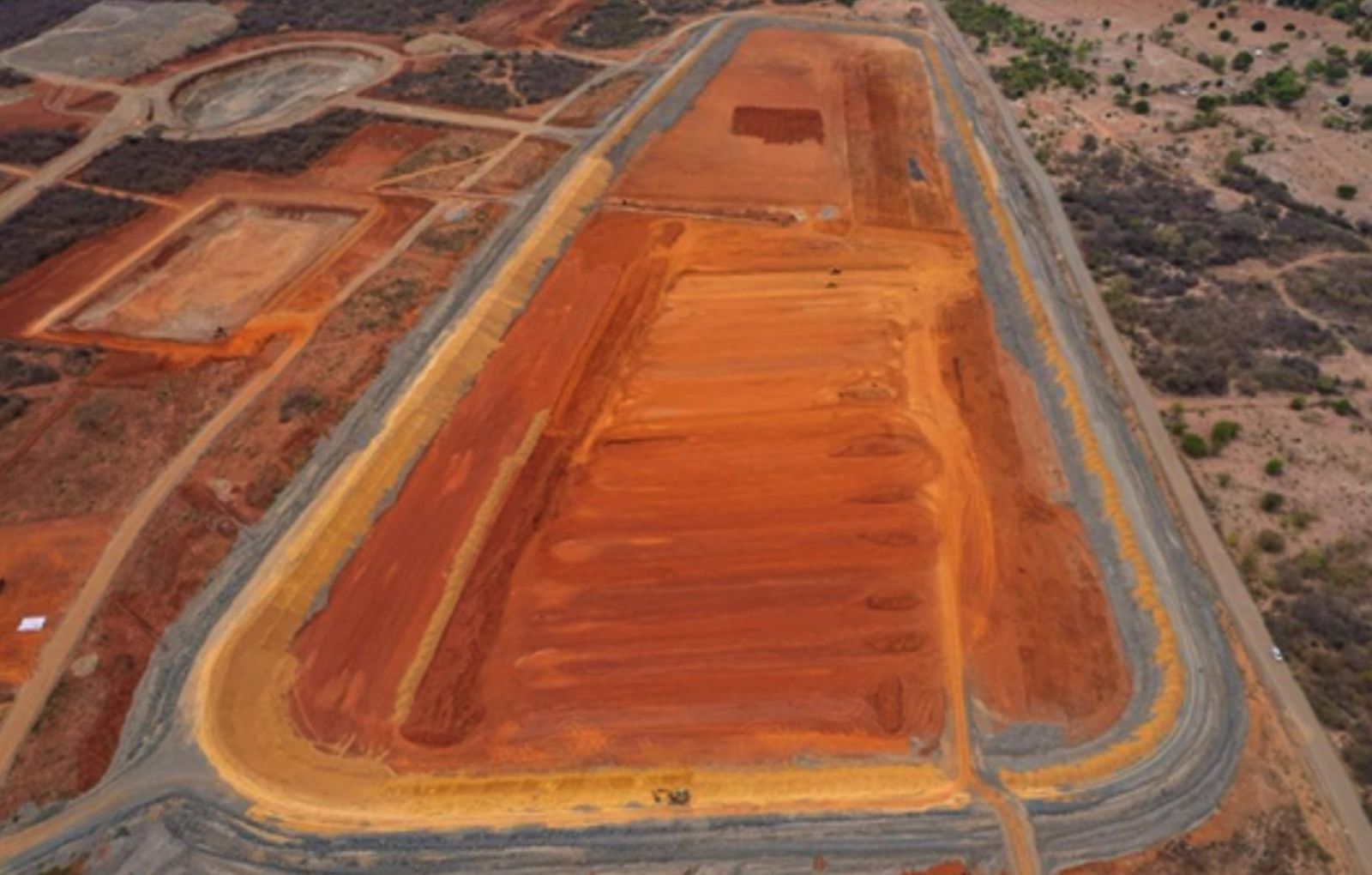 Aerial view of a tailings storage facility under construction, with an orange earth basin inside a grey perimeter embankment and haul roads