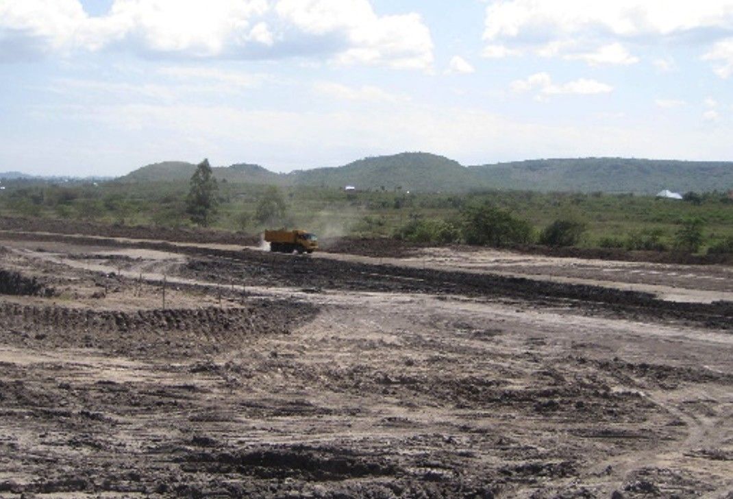A wide area of earthworks under way, with a dump truck in the middle distance and green hills on the horizon