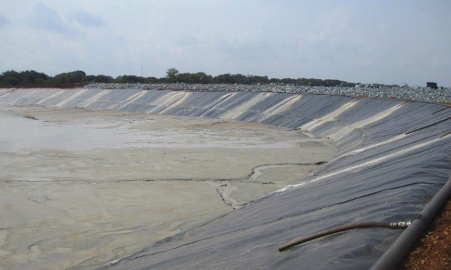 A geomembrane-lined tailings cell with deposited tailings in the basin and a pipeline along the crest