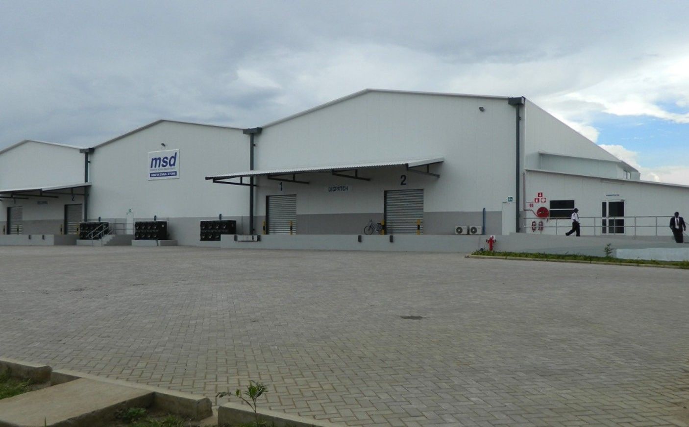 A completed white storage warehouse with MSD branding and numbered loading bays, fronted by a wide block-paved yard