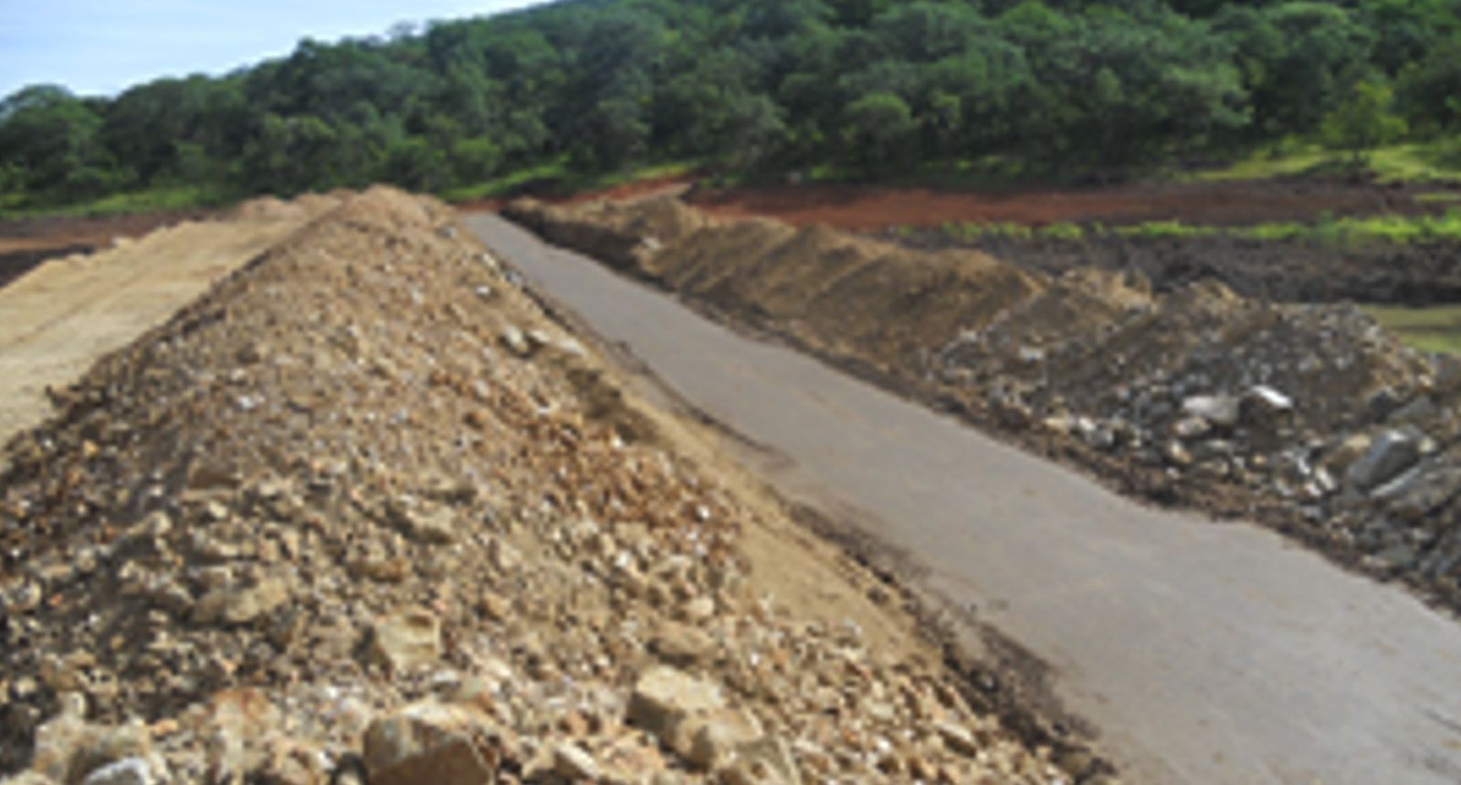 The crest of an earth embankment under construction, with a rockfill slope on one side and a compacted access track along the top