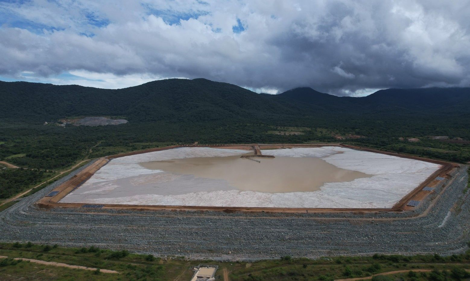 Aerial view of a lined tailings storage facility with a rockfill perimeter embankment, tailings and ponded water in the basin, set among forested hills