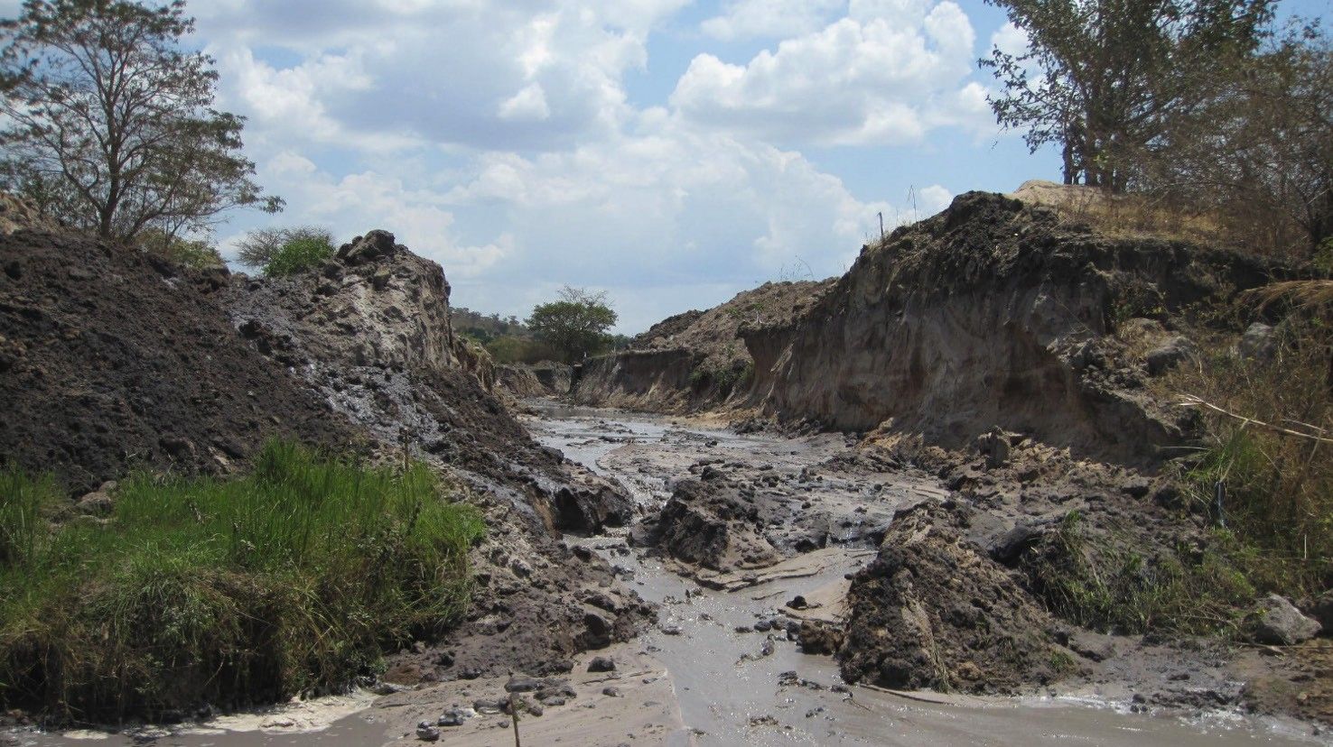 A freshly excavated river channel with steep earth banks and muddy water running along its bed