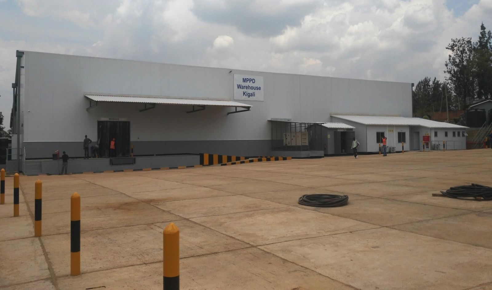 A long white warehouse signed MPPD Warehouse Kigali, with canopied loading doors and a concrete yard lined with yellow and black bollards