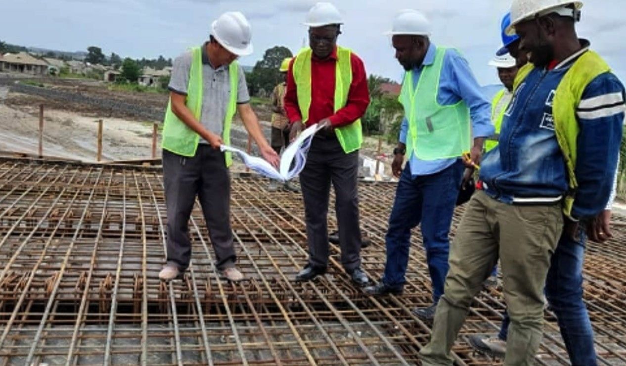 Engineers and site staff in hard hats and high-visibility vests standing on a reinforcement mat, reviewing a set of construction drawings together